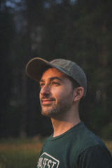 Man wearing a green t-shirt and a hat standing in a field surrounded by trees — sample image to upscale