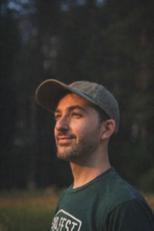Man wearing a green t-shirt and a hat standing in a field surrounded by trees — sample image to upscale