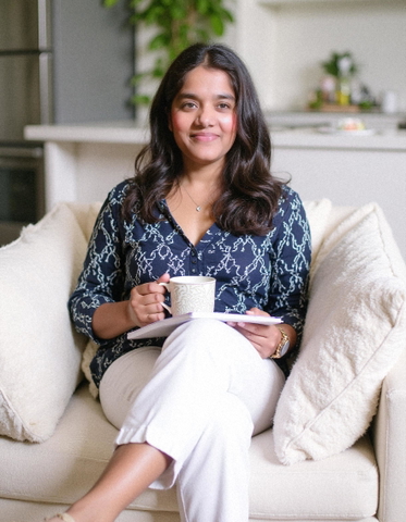 Kanika Bhatt, founder of GoStudio.ai, seated on a cream sofa with a mug and a notebook