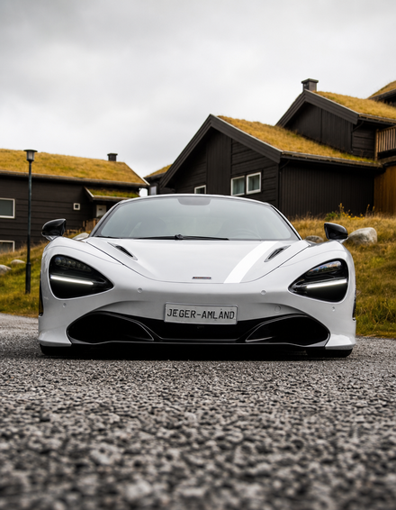 White sports car at ground level, parked on green grass, with houses in the background.