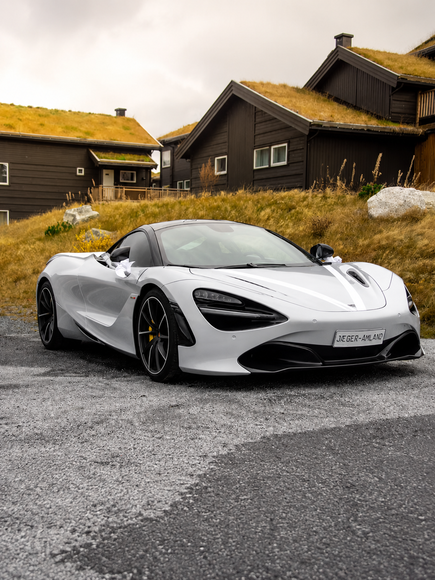 White sports car parked in front of a house with a green roof, surrounded by grass and rocks, with sky in the background. Original uploaded car photo. White sports car parked in front of a house with a green roof, surrounded by grass and rocks, with sky in the background. Original uploaded car photo.
