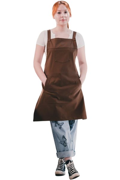 A woman in a brown apron standing in a bright cafe — background removed by iLoveIMG