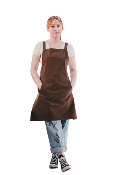 A woman in a brown apron standing in a bright cafe — background removed by Erase.bg