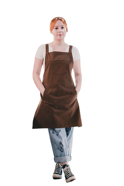 A woman in a brown apron standing in a bright cafe — background removed by Photoroom