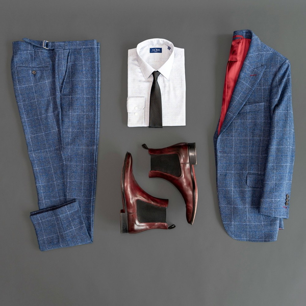A blue checked suit laid out flat with a shirt, tie and boots
