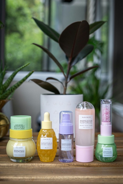 A shelf of pastel skincare bottles in front of houseplants