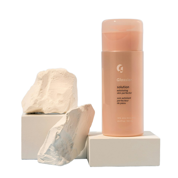 A pink cosmetic bottle balanced on a stone plinth — background removed by Photoroom