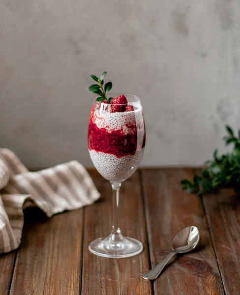 A berry parfait in a tall glass beside a spoon