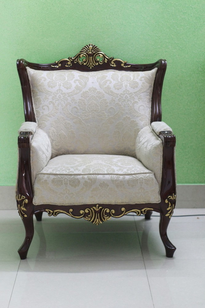 An ornate carved armchair against a green wall