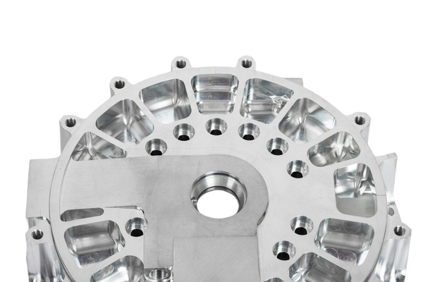 A machined aluminium housing with bolt holes — background removed by Photoroom