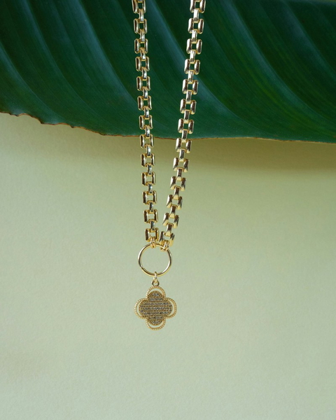 A gold chain necklace with a pendant, lying on a green leaf