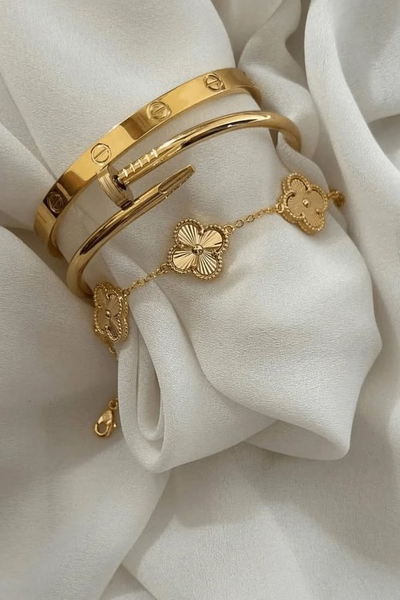 Two gold bangles and a clover-motif bracelet resting on draped white silk