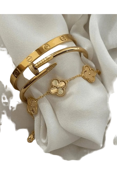 Two gold bangles and a clover-motif bracelet resting on draped white silk — background removed by iLoveIMG