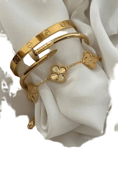 Two gold bangles and a clover-motif bracelet resting on draped white silk — background removed by GoStudio.ai (Free)