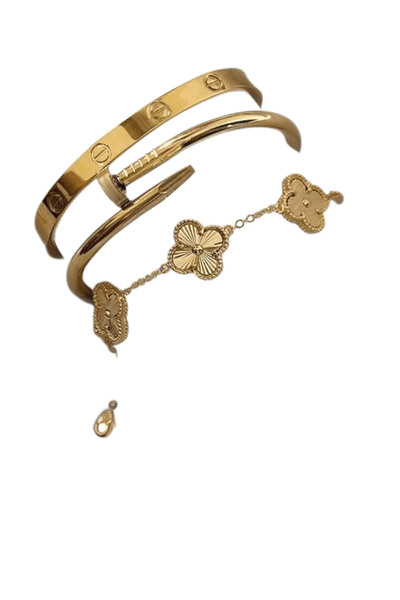 Two gold bangles and a clover-motif bracelet resting on draped white silk — background removed by Remove.bg
