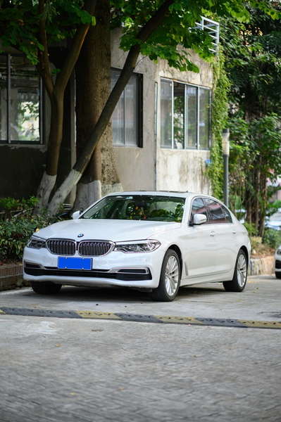 A white saloon car parked on a tree-lined street