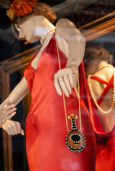 Shop mannequin in an orange dress with a pendant necklace, seen through glass — upscaled by GoStudio Advanced