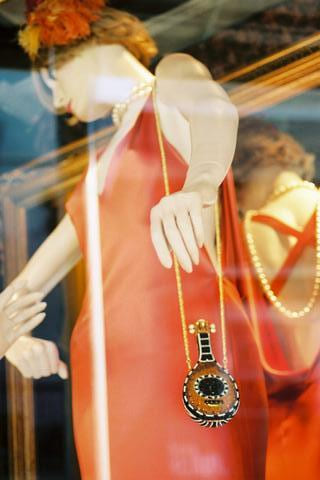 Shop mannequin in an orange dress with a pendant necklace, seen through glass
