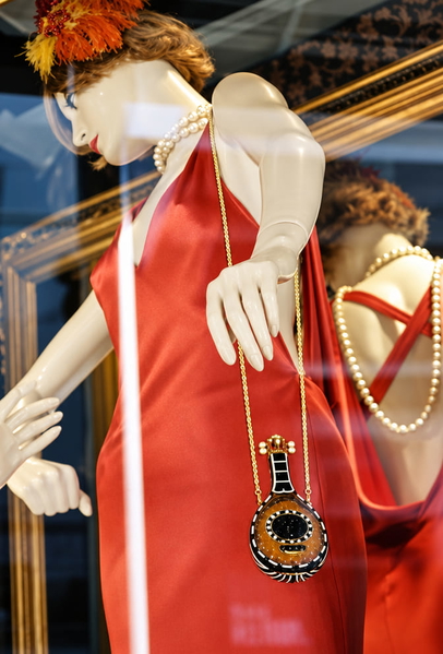 Shop mannequin in an orange dress with a pendant necklace, seen through glass — upscaled by GPT Image 2.5