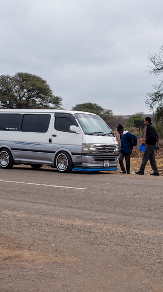 White van on a dirt road with two people standing beside it — upscaled by GoStudio Advanced