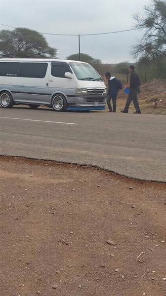 White van on a dirt road with two people standing beside it — upscaled by GoStudio Lite
