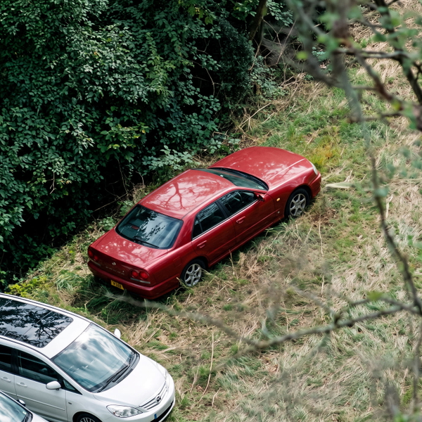 Aerial view of a red car on grass beside a road — upscaled by GoStudio Advanced