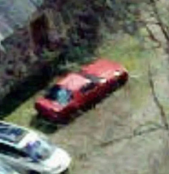 Aerial view of a red car on grass beside a road