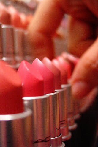 Row of pink and red lipsticks with a hand reaching in, shallow depth of field