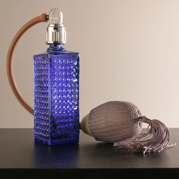 Blue cut-glass perfume atomiser with a tasselled bulb on a dark table — upscaled by GoStudio Advanced