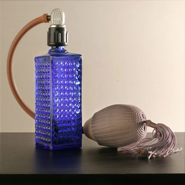 Blue cut-glass perfume atomiser with a tasselled bulb on a dark table — upscaled by GoStudio Lite
