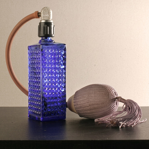 Blue cut-glass perfume atomiser with a tasselled bulb on a dark table — upscaled by Nano Banana 2