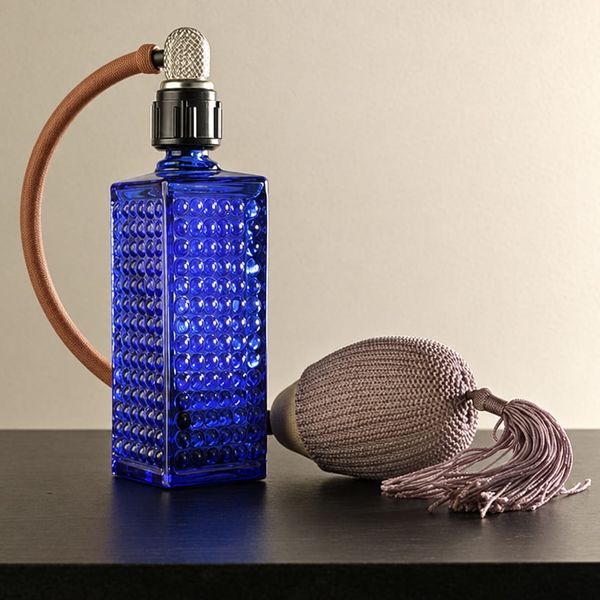 Blue cut-glass perfume atomiser with a tasselled bulb on a dark table — upscaled by GPT Image 2.5