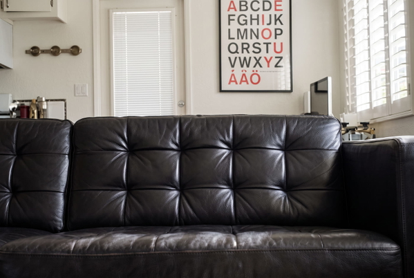 Black tufted leather sofa in front of a wall with an alphabet poster — upscaled by GoStudio Advanced
