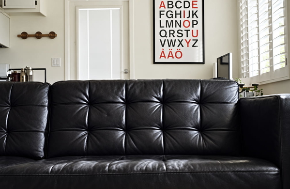 Black tufted leather sofa in front of a wall with an alphabet poster — upscaled by GPT Image 2.5