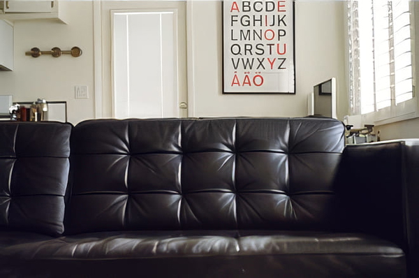 Black tufted leather sofa in front of a wall with an alphabet poster — upscaled by GoStudio Pro