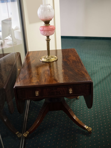 Mahogany drop-leaf table with a brass oil lamp on a green carpet — upscaled by GoStudio Advanced