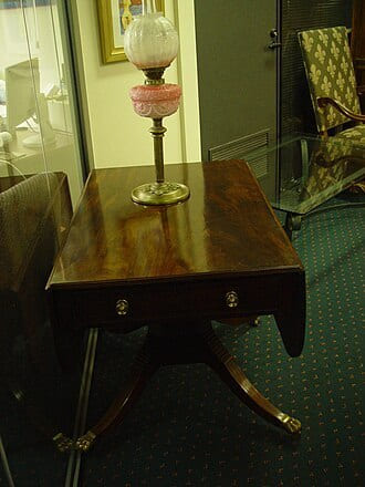 Mahogany drop-leaf table with a brass oil lamp on a green carpet