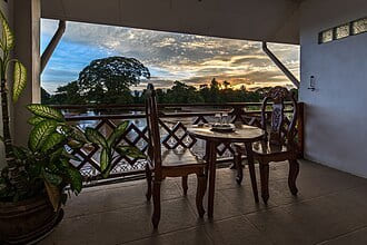 Balcony with carved wooden chairs and a table overlooking a river at sunset