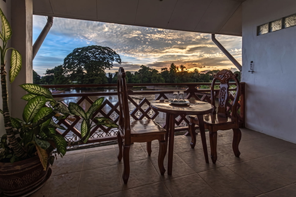 Balcony with carved wooden chairs and a table overlooking a river at sunset — upscaled by Nano Banana 2