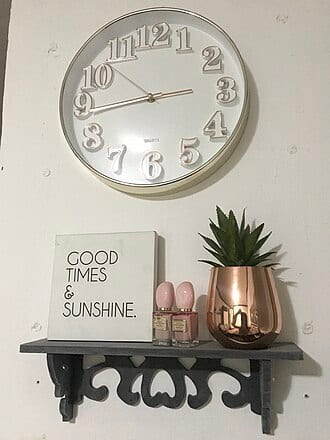 Wall clock above a shelf with a "Good times & sunshine" sign and a succulent