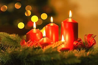 Red candles lit on a pine garland with bokeh lights behind