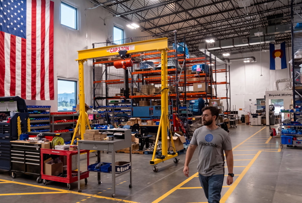 Fabrication workshop with a yellow gantry crane, storage racking and a US flag on the wall — upscaled by GoStudio Advanced
