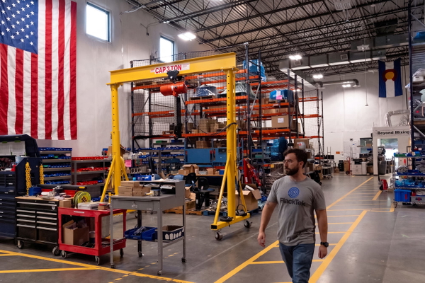 Fabrication workshop with a yellow gantry crane, storage racking and a US flag on the wall — upscaled by Nano Banana 2