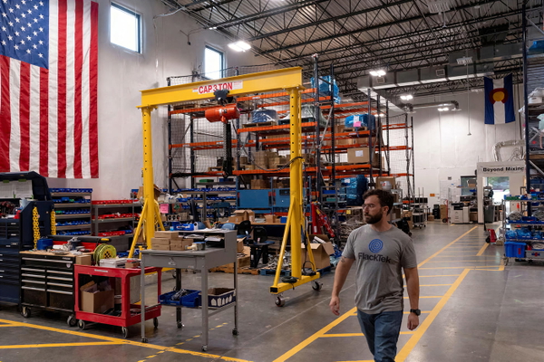 Fabrication workshop with a yellow gantry crane, storage racking and a US flag on the wall — upscaled by GoStudio Pro