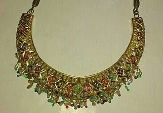 Gold collar necklace set with coloured stones on a pale background