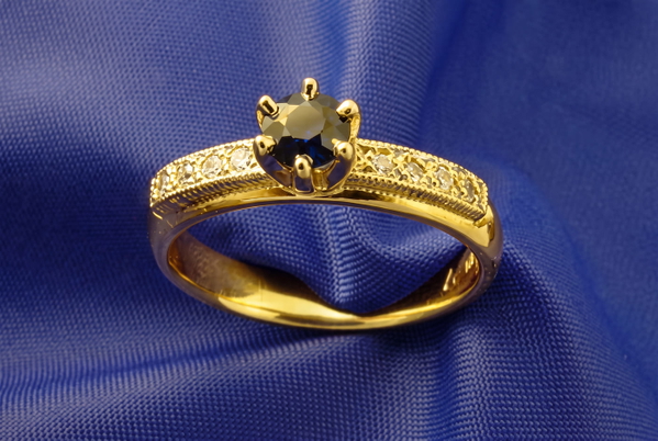 Gold ring with a dark faceted stone resting on blue satin — upscaled by GoStudio Advanced