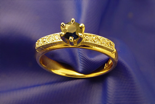 Gold ring with a dark faceted stone resting on blue satin — upscaled by GoStudio Lite