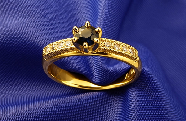 Gold ring with a dark faceted stone resting on blue satin — upscaled by GPT Image 2.5