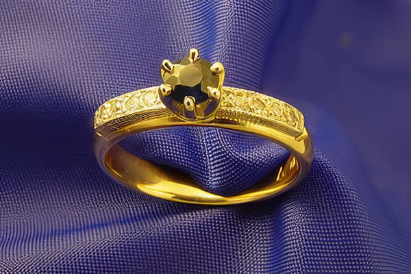Gold ring with a dark faceted stone resting on blue satin — upscaled by GoStudio Pro