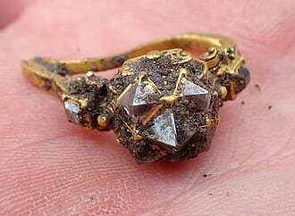 Rough uncut diamond set in a gold ring, held on a fingertip